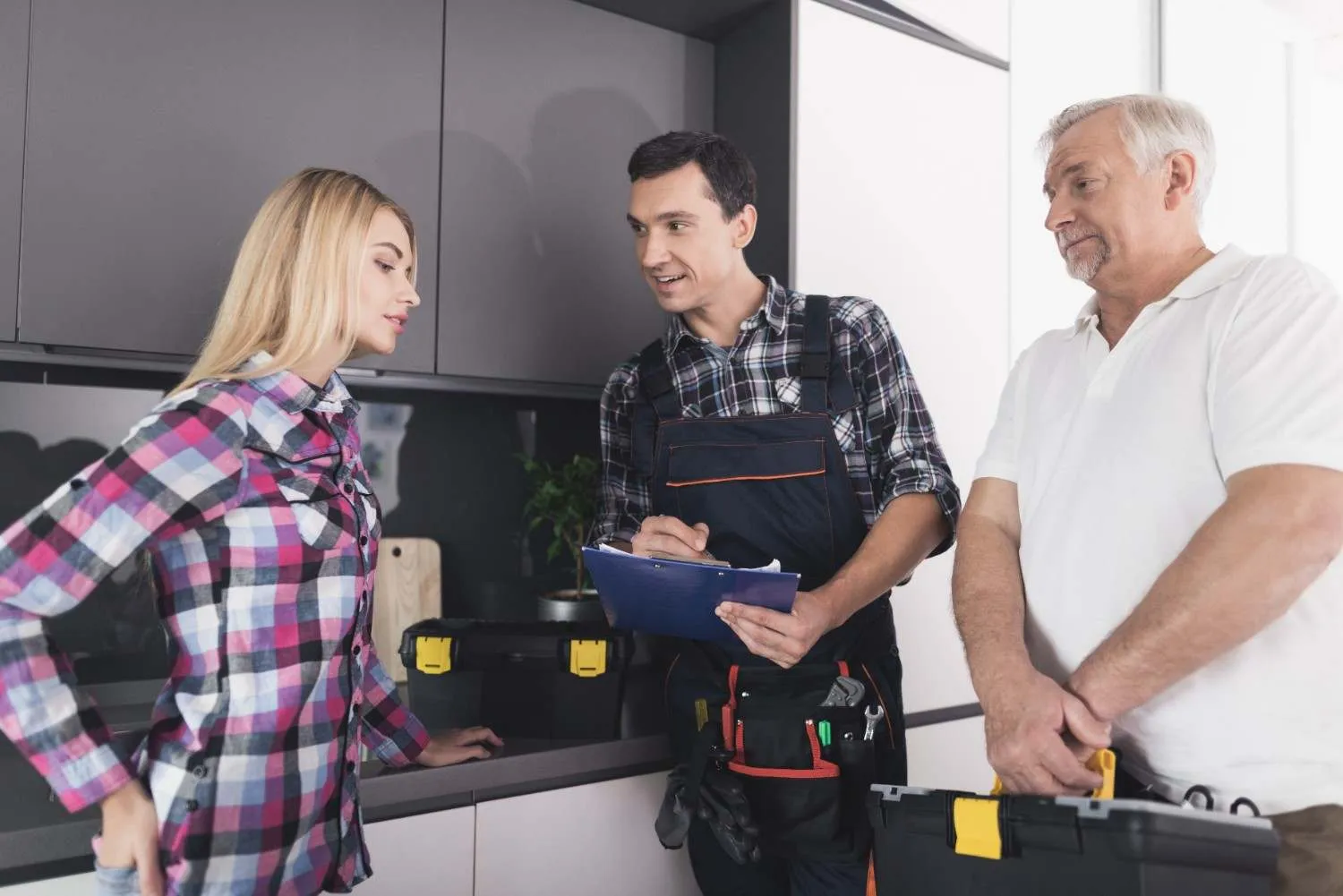 Technician with a clipboard talking with two homeowners in their kitchen